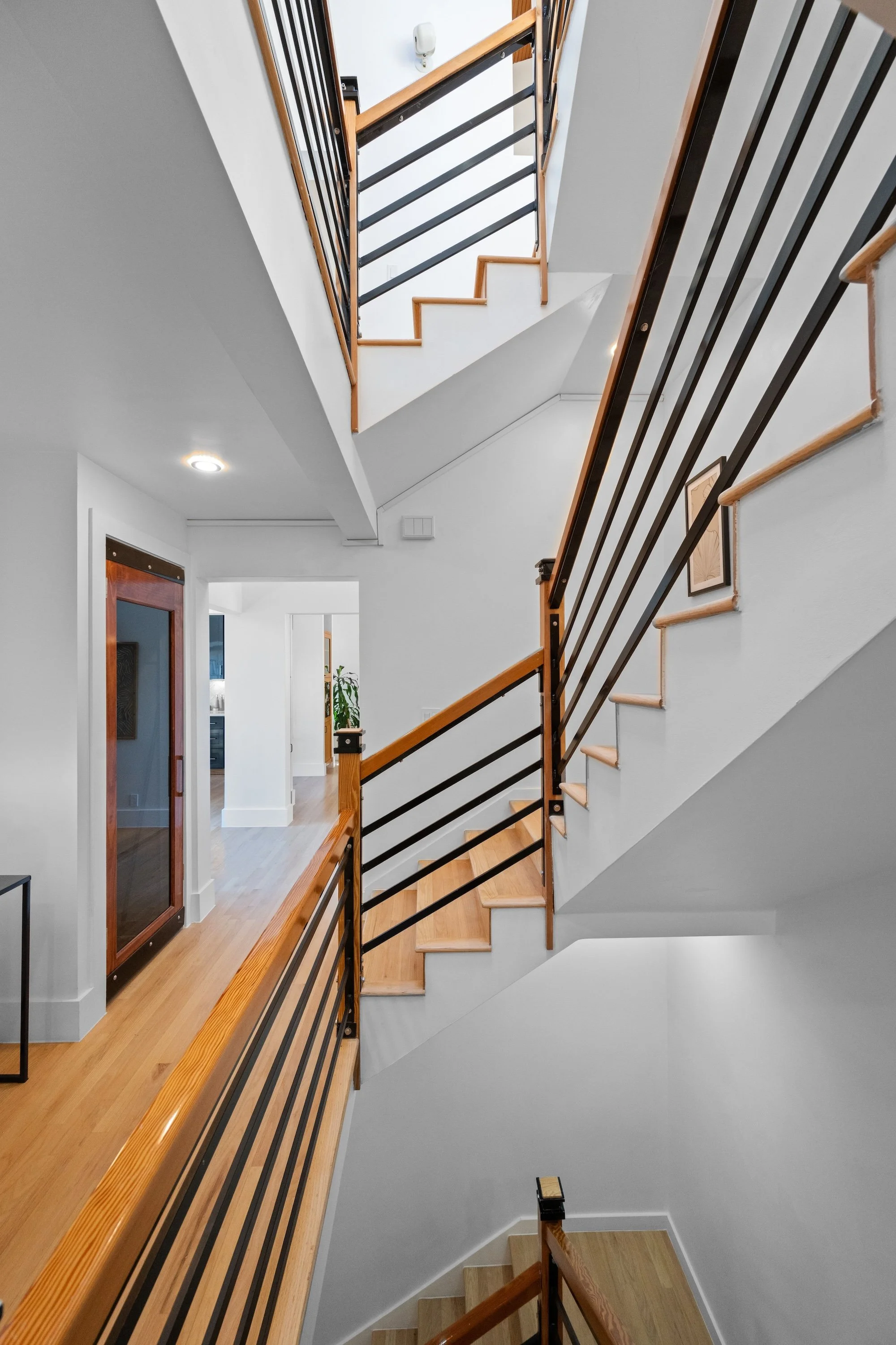View of a staircase with wooden and metal railings inside a residential home, with a hallway and doorway visible in the background.