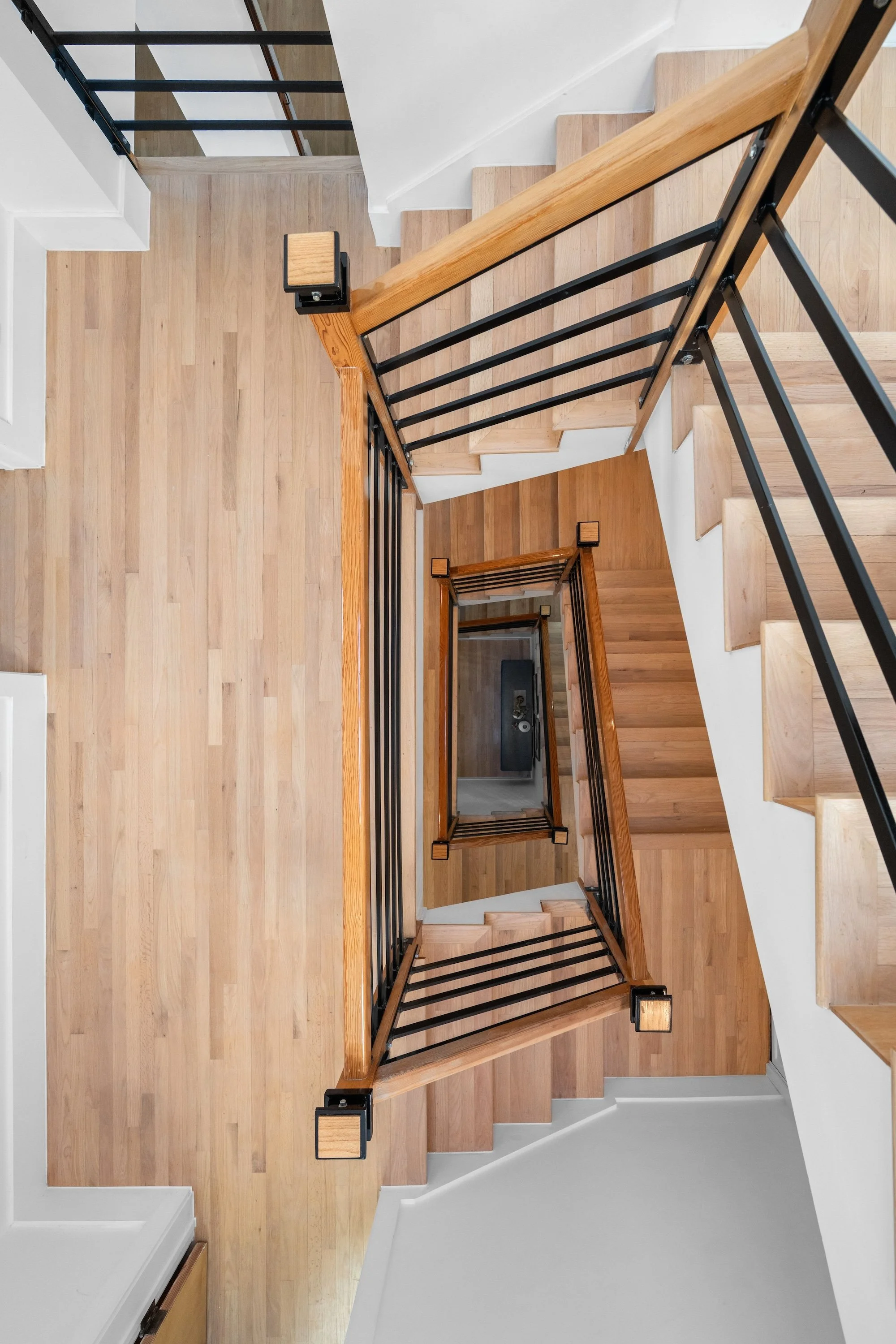 View of a staircase with wooden steps, black metal railings, and wooden handrails, viewed from above.