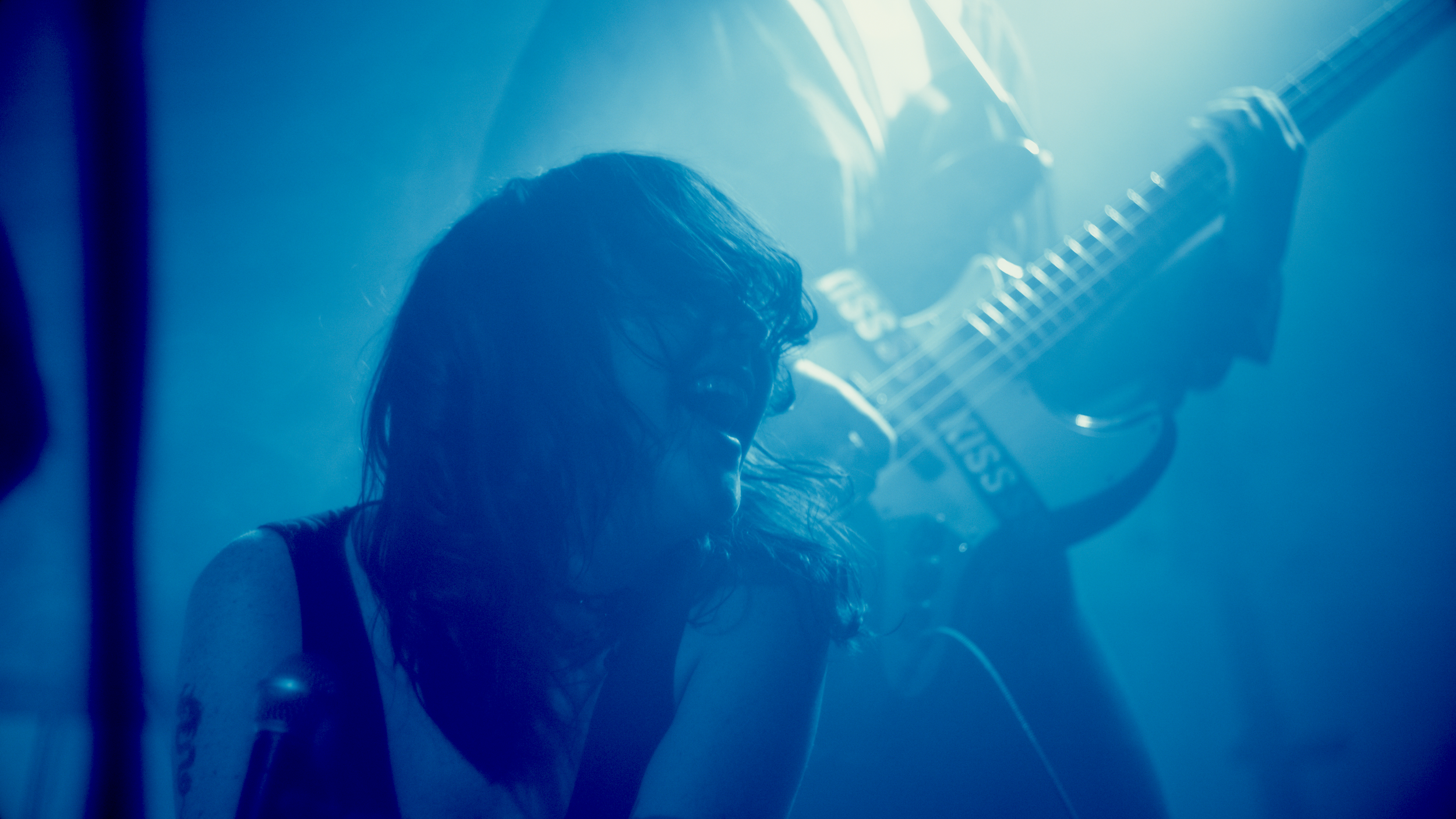 A woman with curly hair playing a guitar, with blue lighting and a foggy atmosphere.