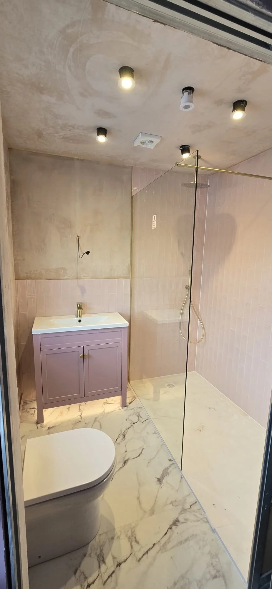Modern bathroom featuring a purple vanity with a white sink, a glass shower area with pink tiled walls. Installed by Chris Murphy Plumbing and Heating 2026
