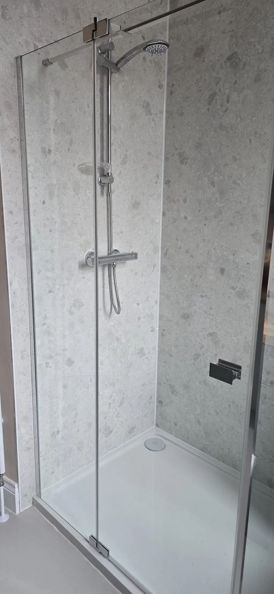A modern shower stall with clear glass doors, a rainfall showerhead, a handheld shower, on a light-colored tiled wall. Installed by Chris Murphy Plumbing and Heating 2026