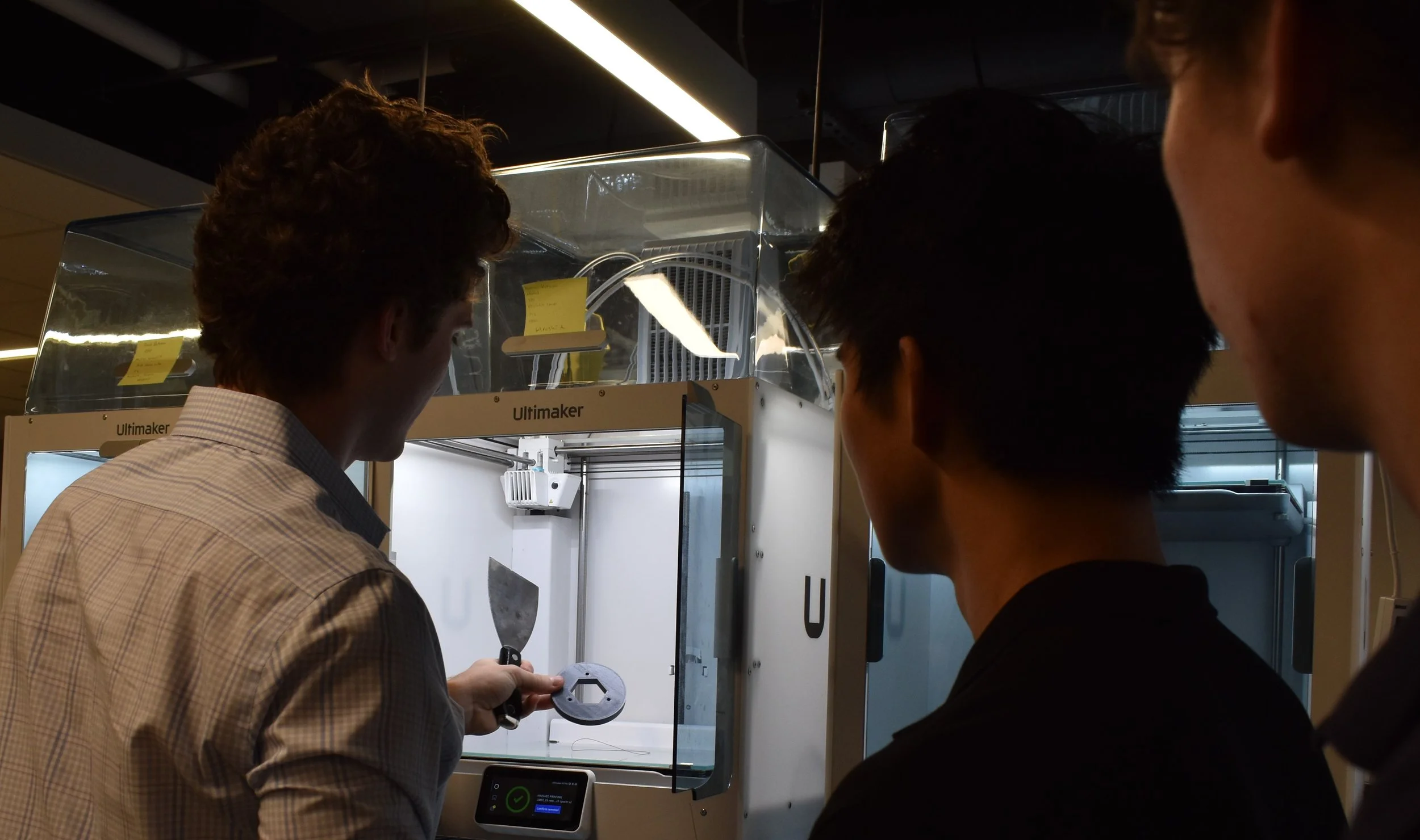 Three men are gathered around a microscope in a laboratory or research setting, examining a small object.