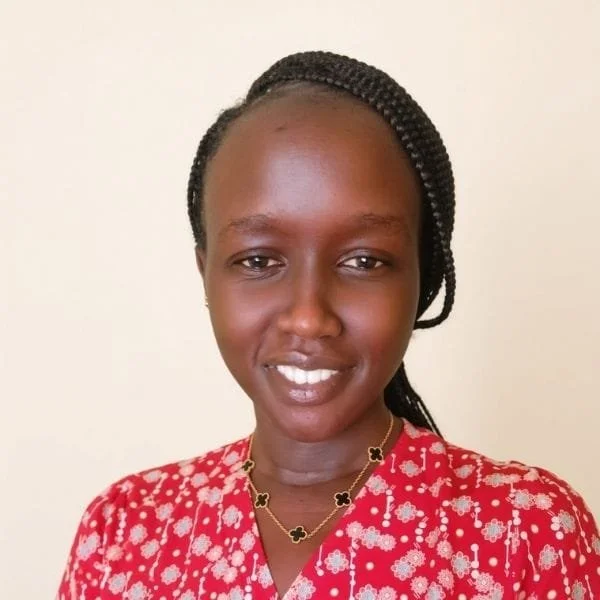 A woman with braided hair wearing a red blouse with white floral patterns, smiling.