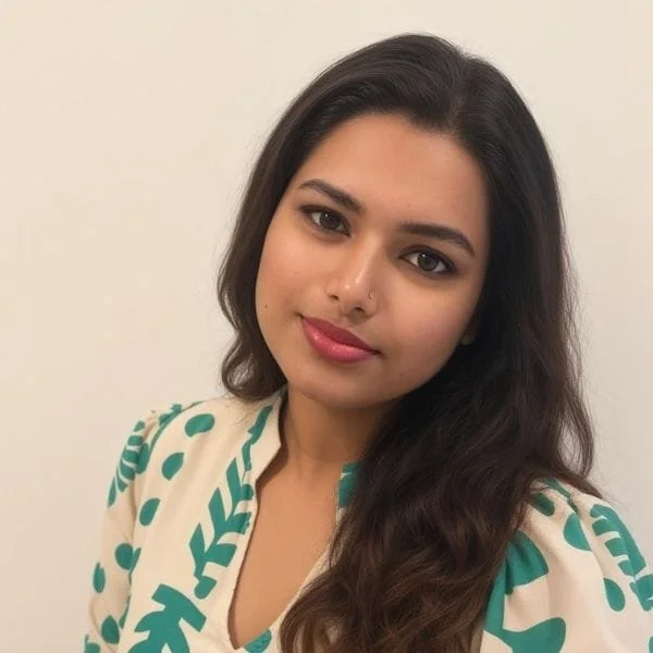 A young woman with long dark hair, wearing a beige and green patterned top, smiling softly at the camera.