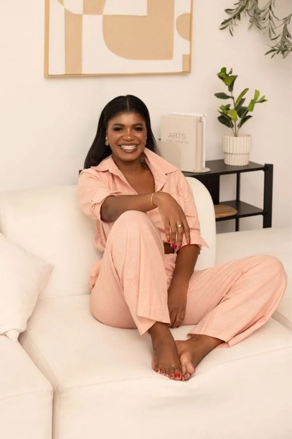 Mercy de-Graft Savage sitting on a white sofa, smiling at the camera, wearing a light pink outfit.