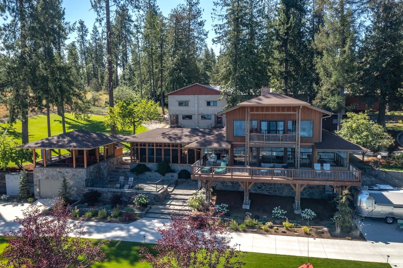 A large multi-story house with extensive outdoor decks and a landscaped yard surrounded by trees.