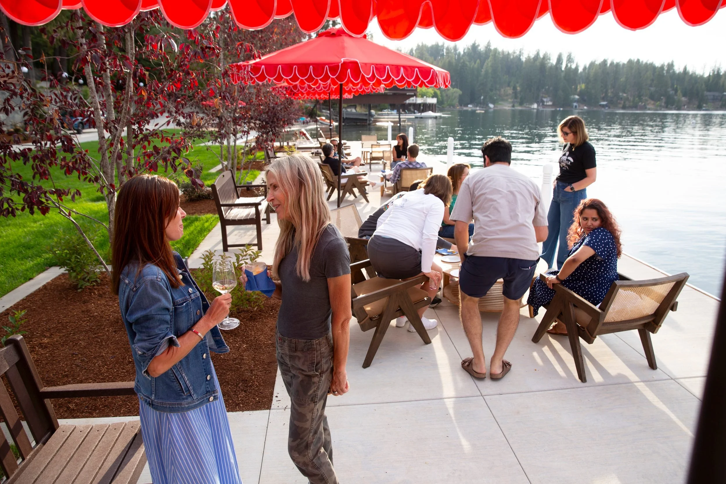 Guests visiting on the lakefront patio under red umbrellas at The Retreat on Lake Pend Oreille