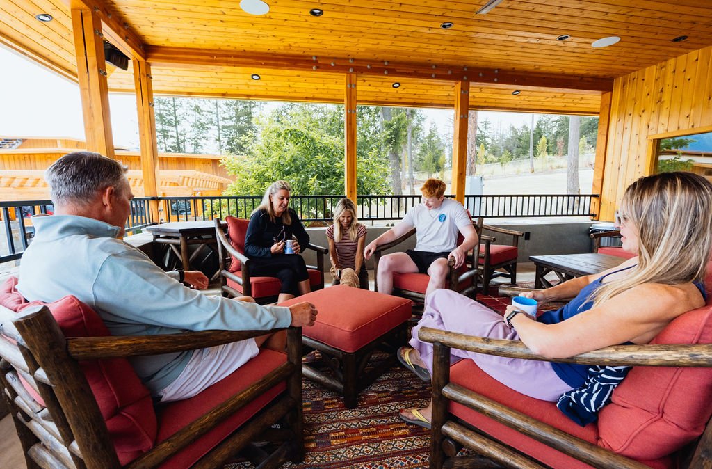 Five guests in conversation on the covered deck at The Retreat on Lake Pend Oreille