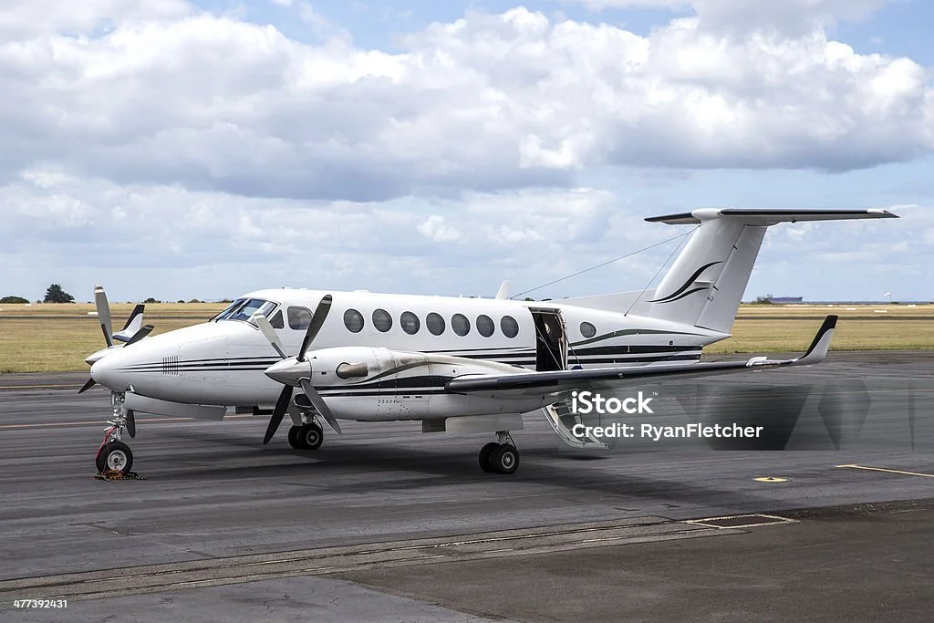 A white private jet parked on an airport tarmac with a cloudy sky in the background.