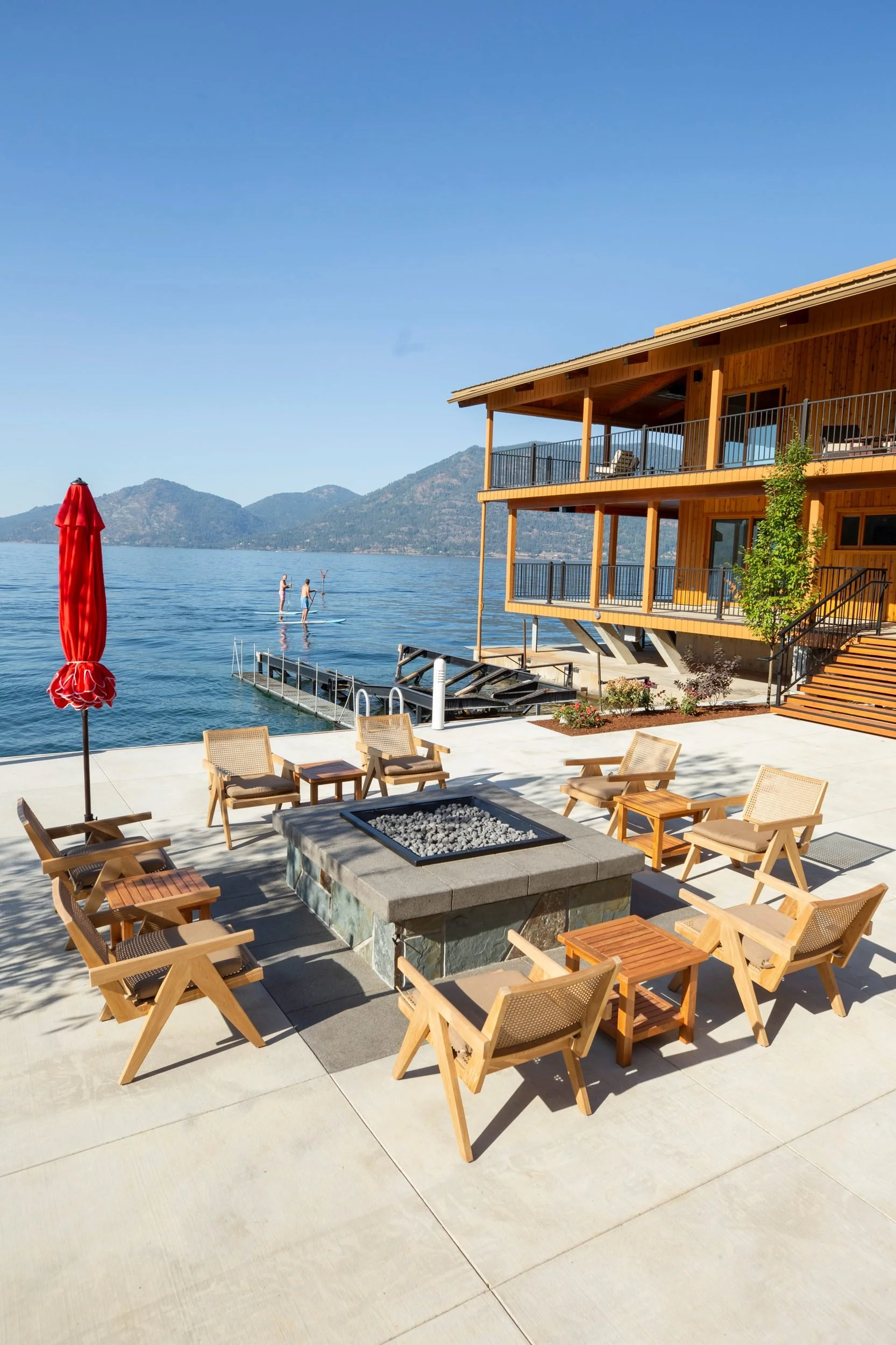 Chairs around the fire pit with paddleboarders beyond on Lake Pend Oreille in Sagle, Idaho