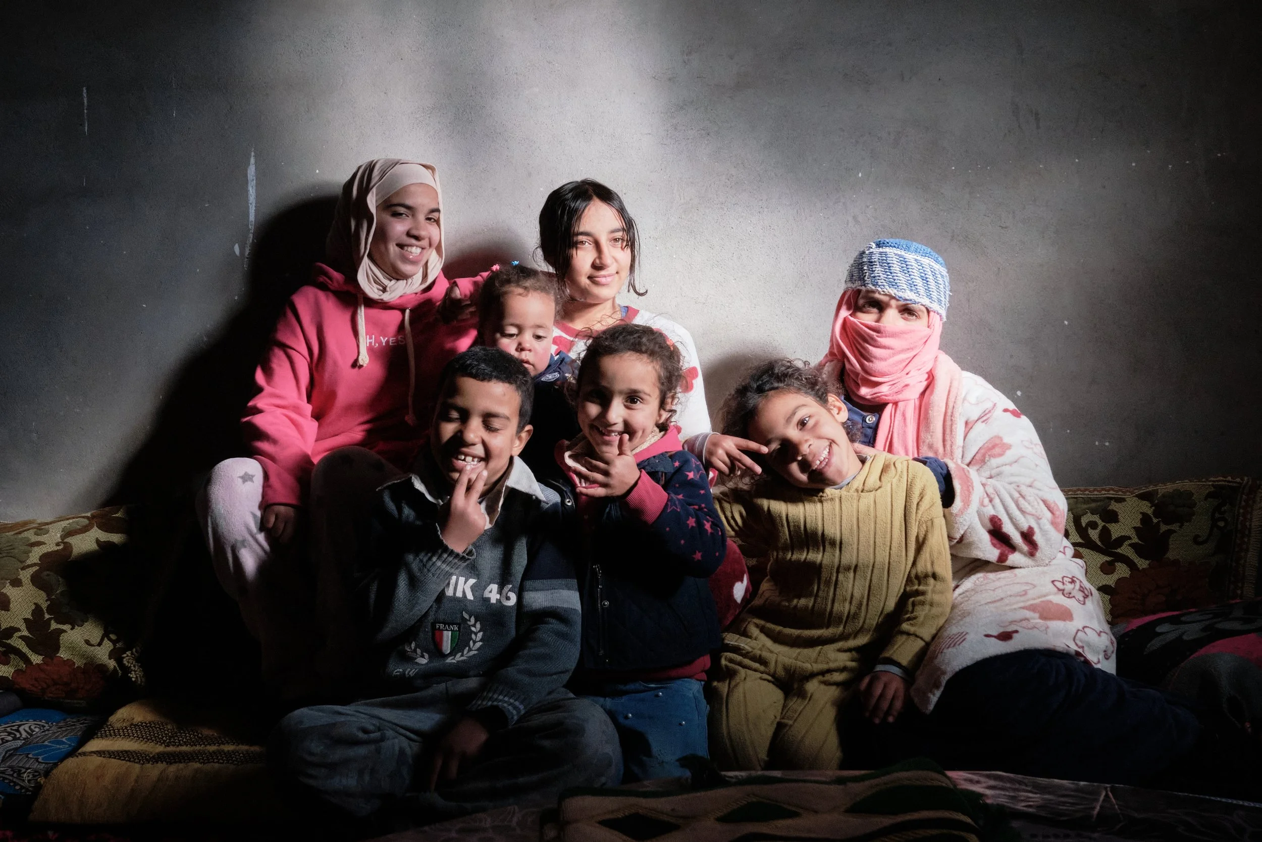 Gruppo di bambini e due adulti seduti su un divano, sorridenti, in un ambiente domestico. Sono felici e appaiono spensierati.