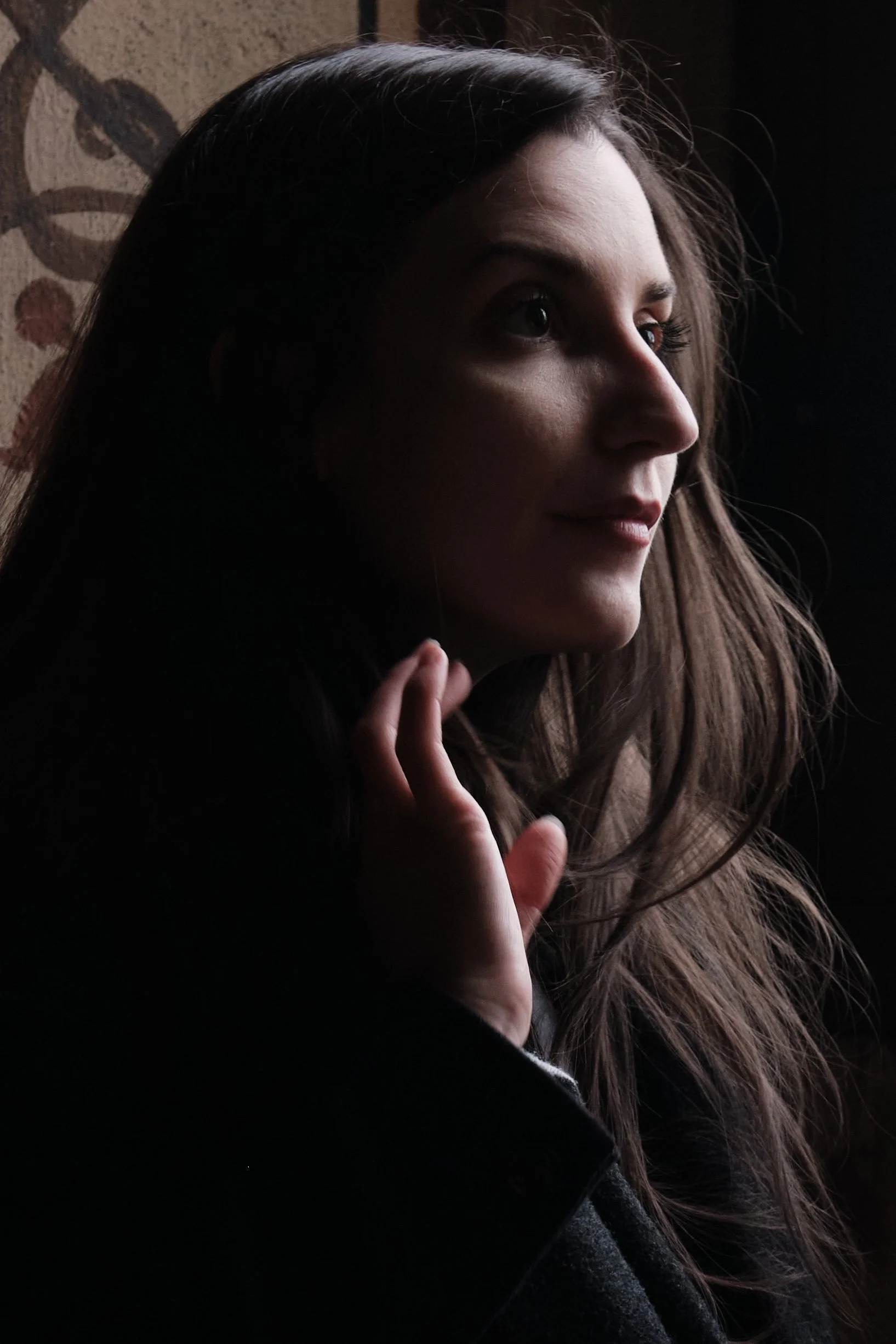 Ritratto di donna con i capelli castani chiusi e viso parzialmente illuminato, sfondo scuro.