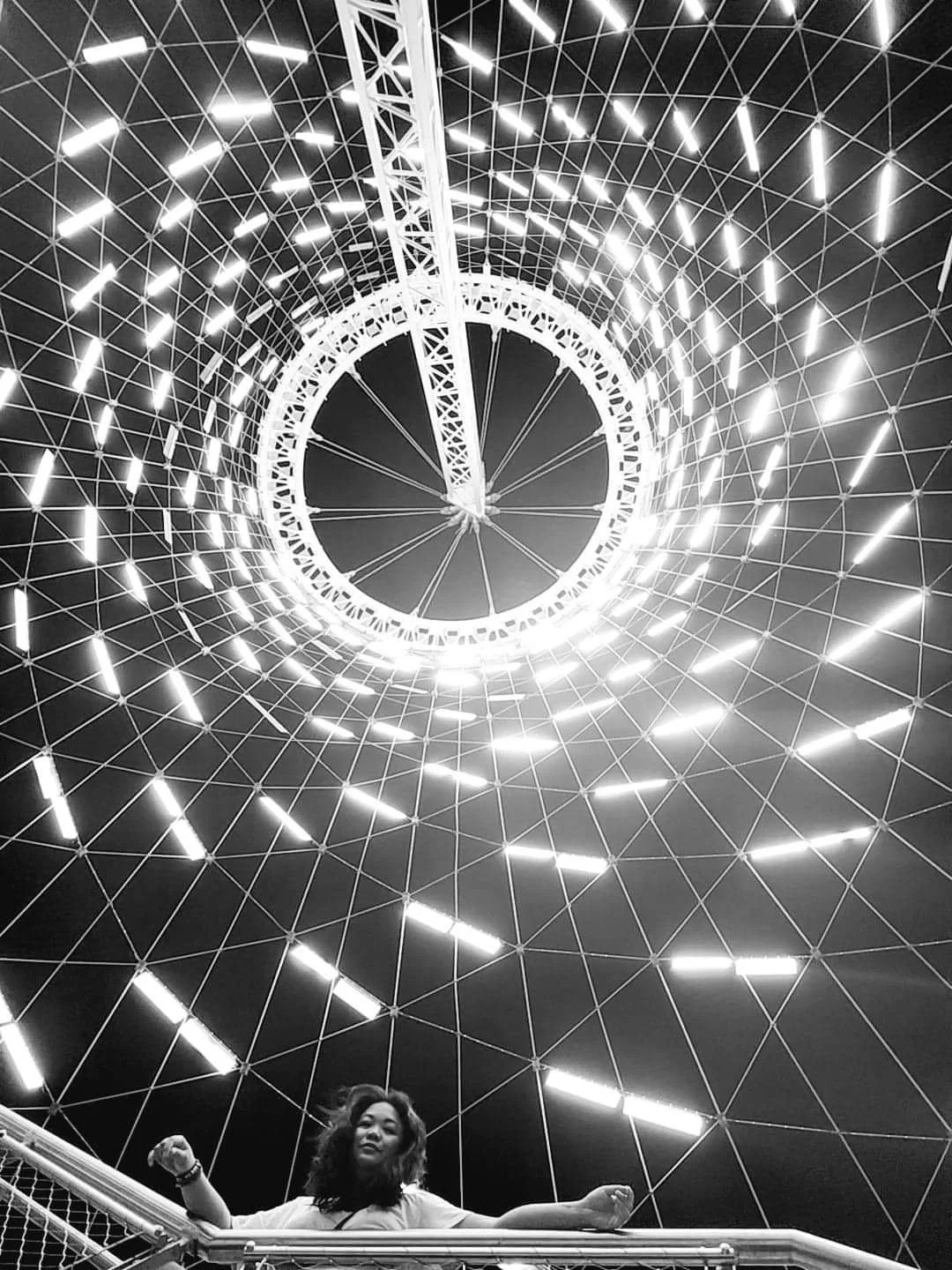 A woman standing on a staircase looking up at the illuminated geometric ceiling of a futuristic structure.