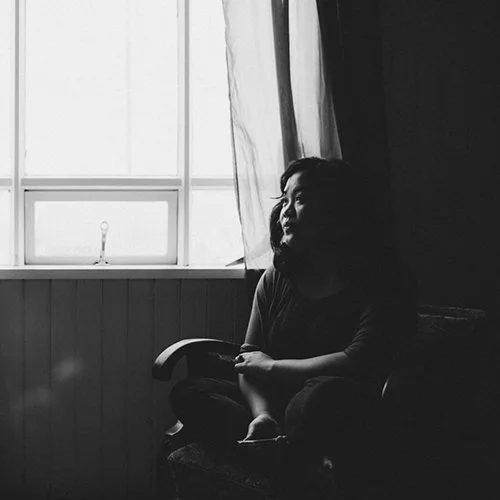 A woman sitting on a chair by a window, with sunlight coming through the window and illuminating her silhouette.