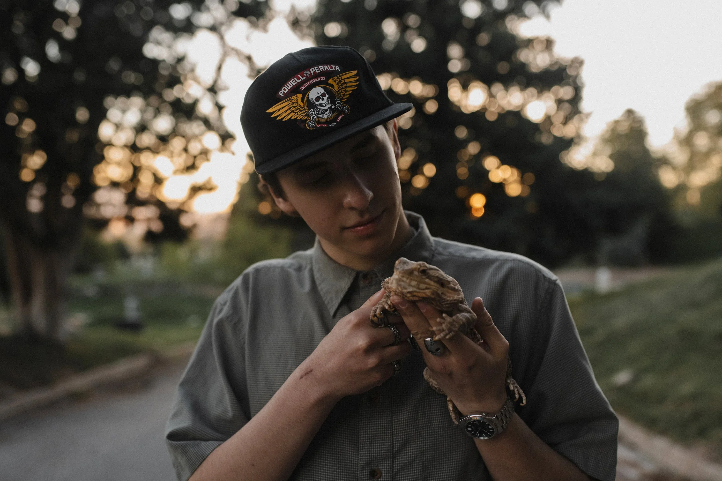 A person wearing a black cap with a skull and wing design holding a bearded dragon.