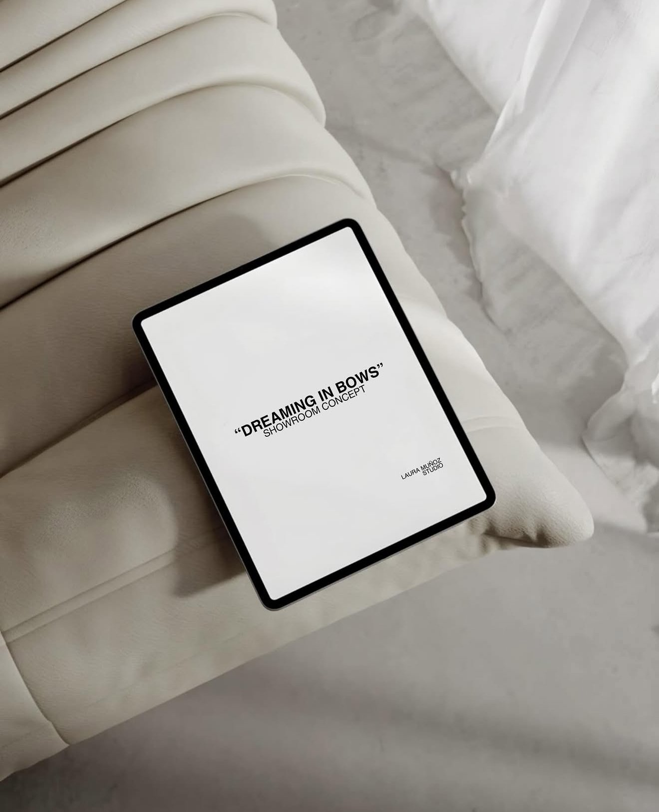 A digital tablet displaying a presentation titled 'Dreaming in Bow's Showroom Concept' by Laura Muñoz Studio. The tablet is resting on a light-colored sofa next to a sheer white curtain.