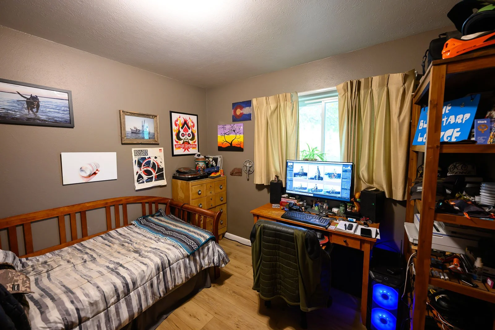 A bedroom with a bed, a desk with a computer monitor, and various decorations and furniture.