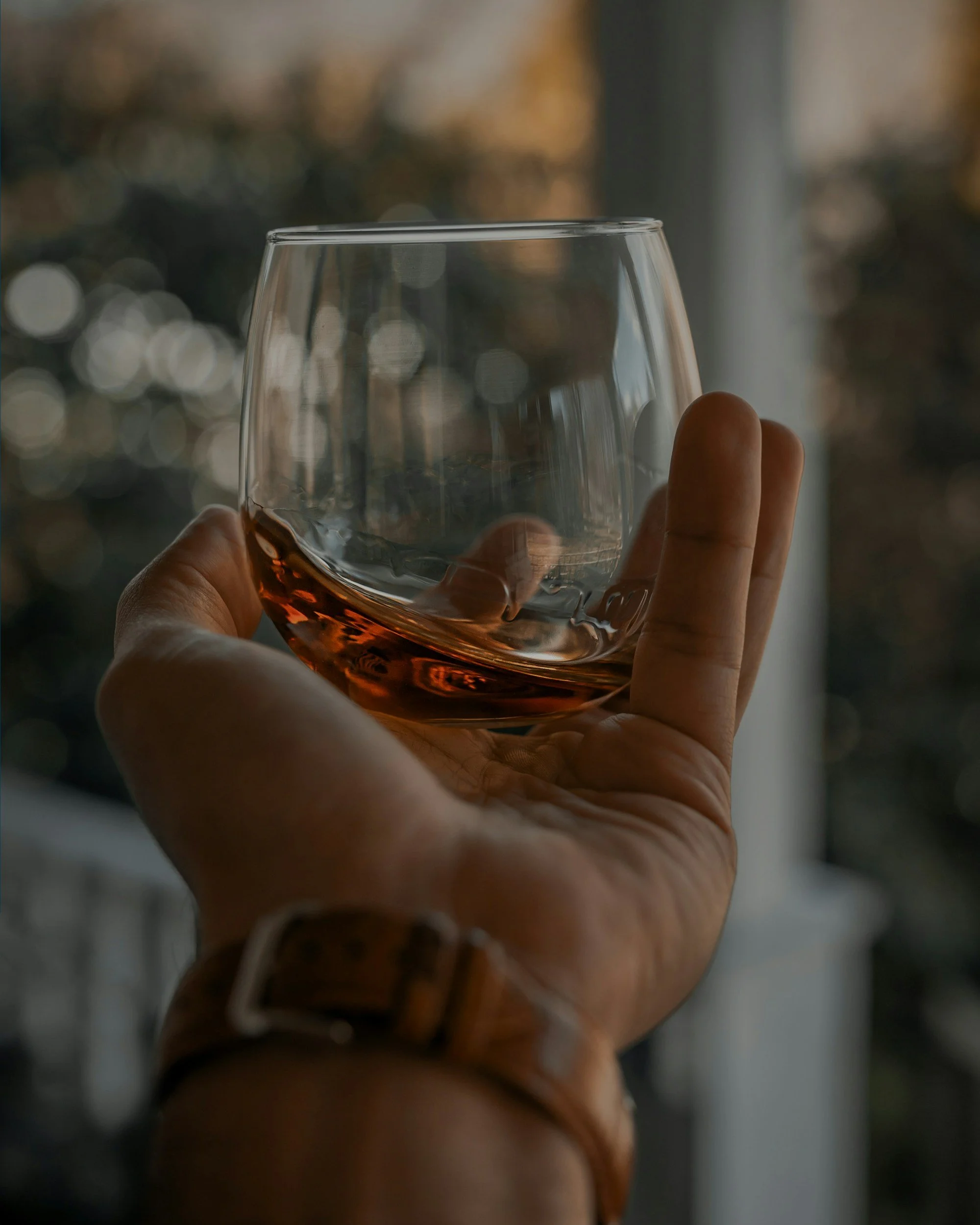 Close-up of a hand holding a glass of whiskey with a blurred background.