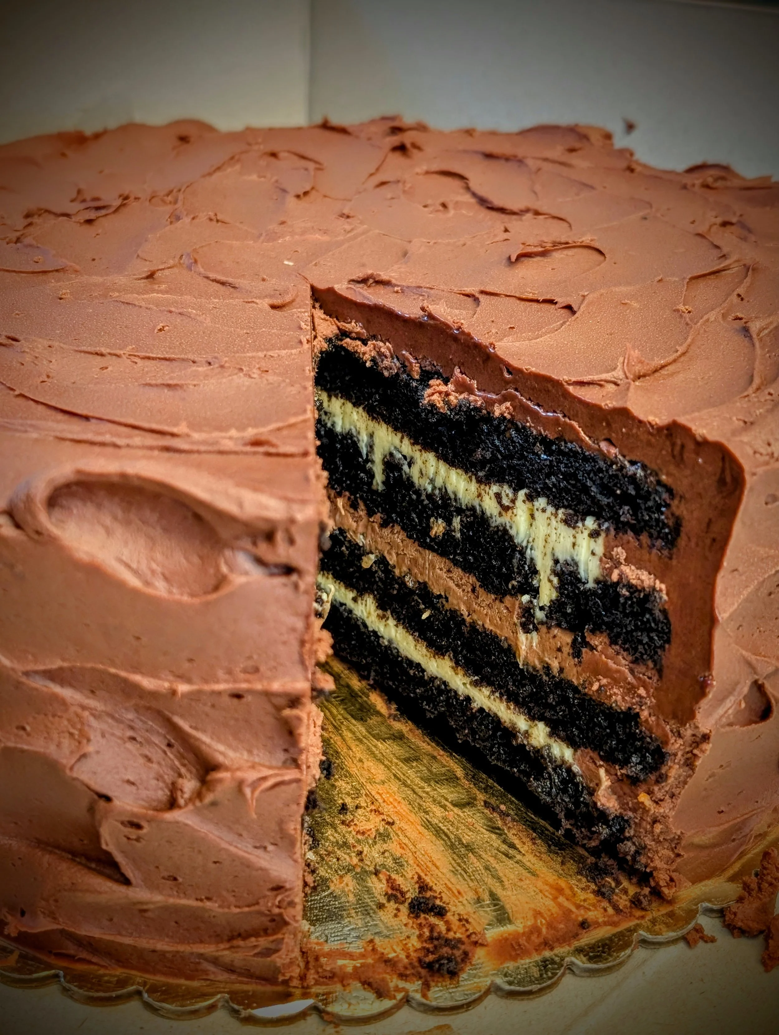 A chocolate layered cake with cream filling and chocolate frosting on top, displayed on a decorative cake stand.