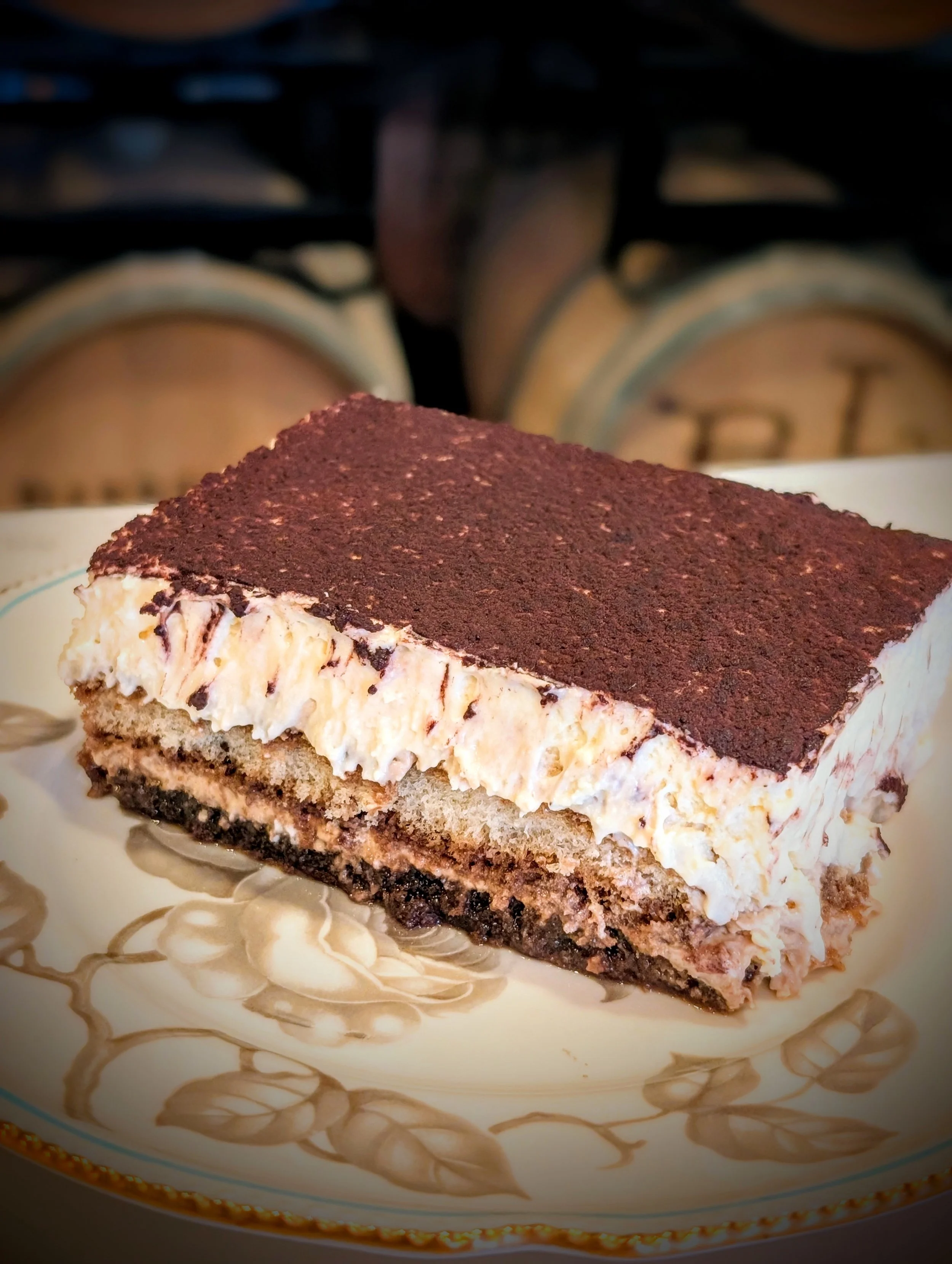A slice of layered dessert with a chocolate top, creamy middle, and cookie crust on a decorative plate.