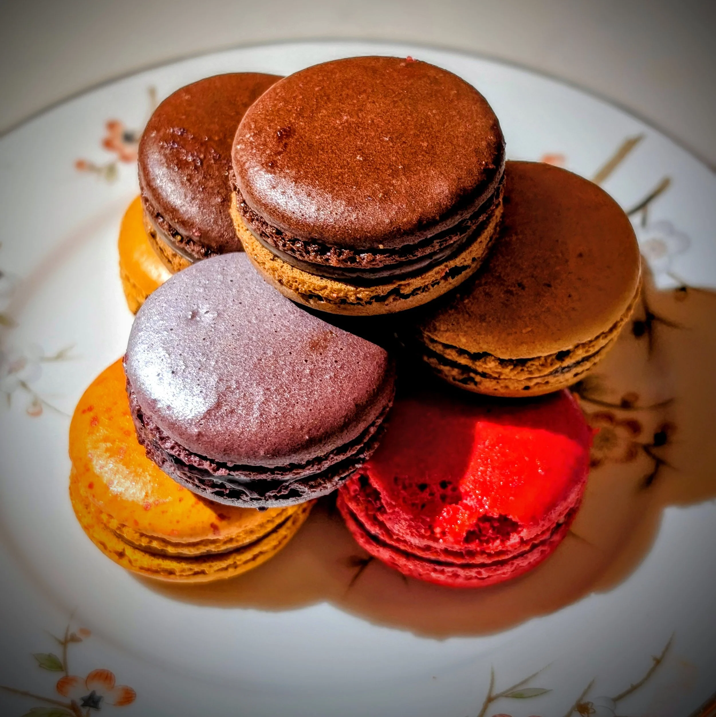 Close-up of assorted macarons on a floral-patterned plate.