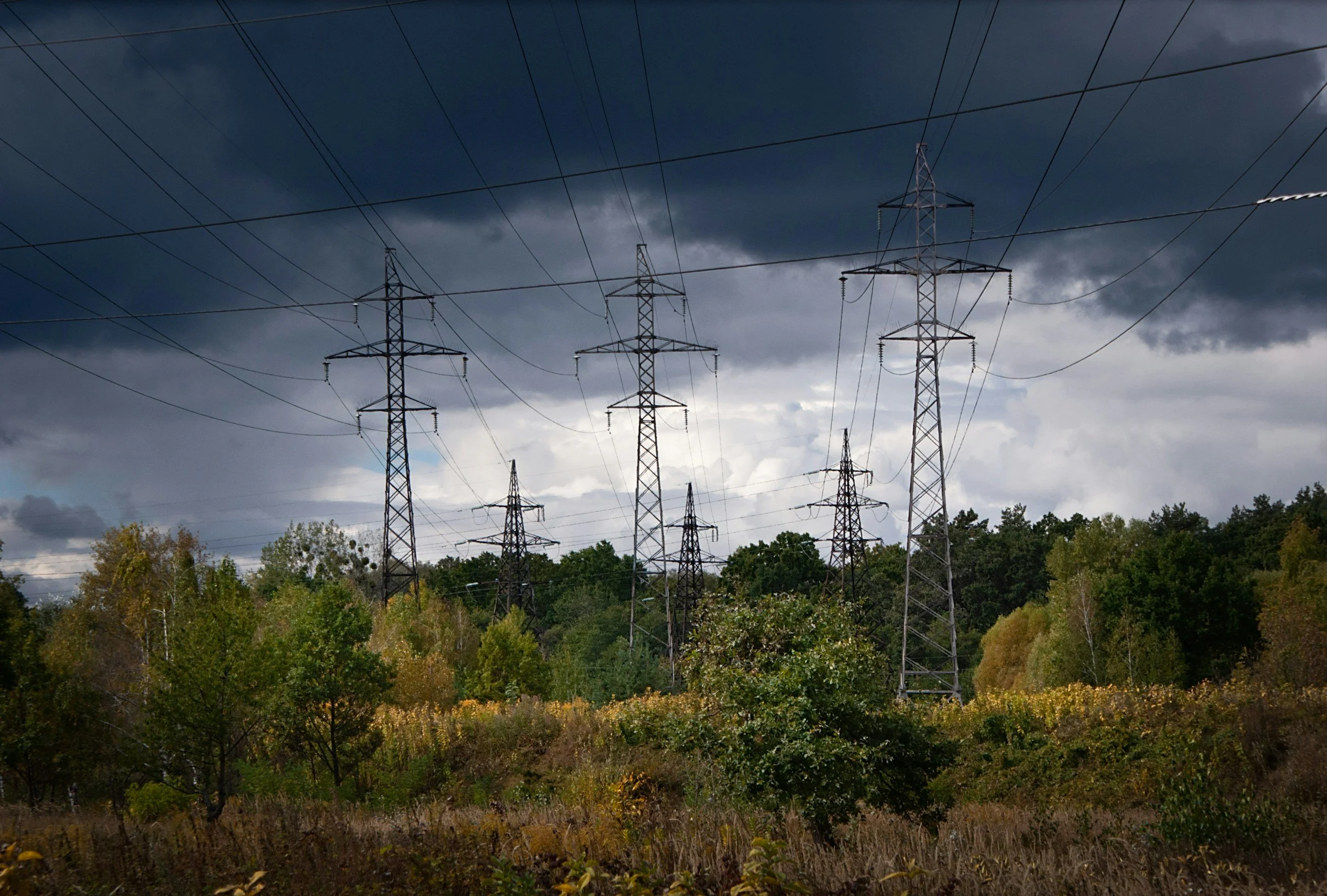 Multiple electrical transmission towers amid a cloudy sky and trees.