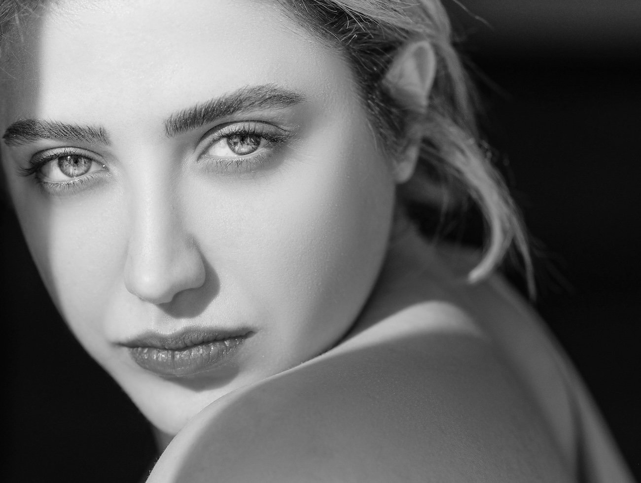 Close-up black and white portrait of a young woman looking at the camera with intense expression.