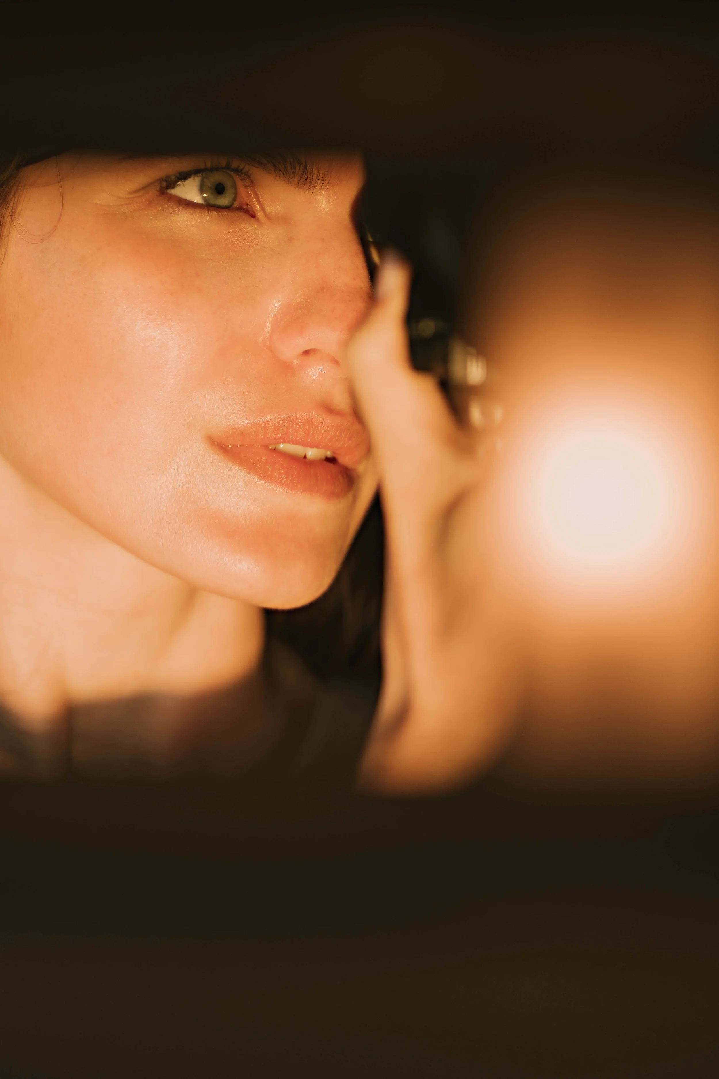 Close-up of a woman's face, focusing on her left eye, nose, and lips, with blurred warm lighting in the background.