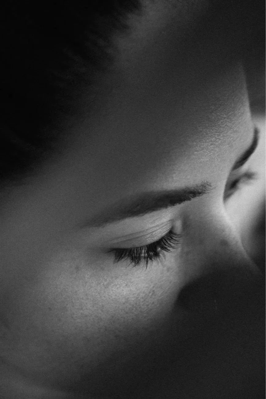 Close-up of a person's face with eyes closed, showcasing long eyelashes and smooth skin, in black and white.
