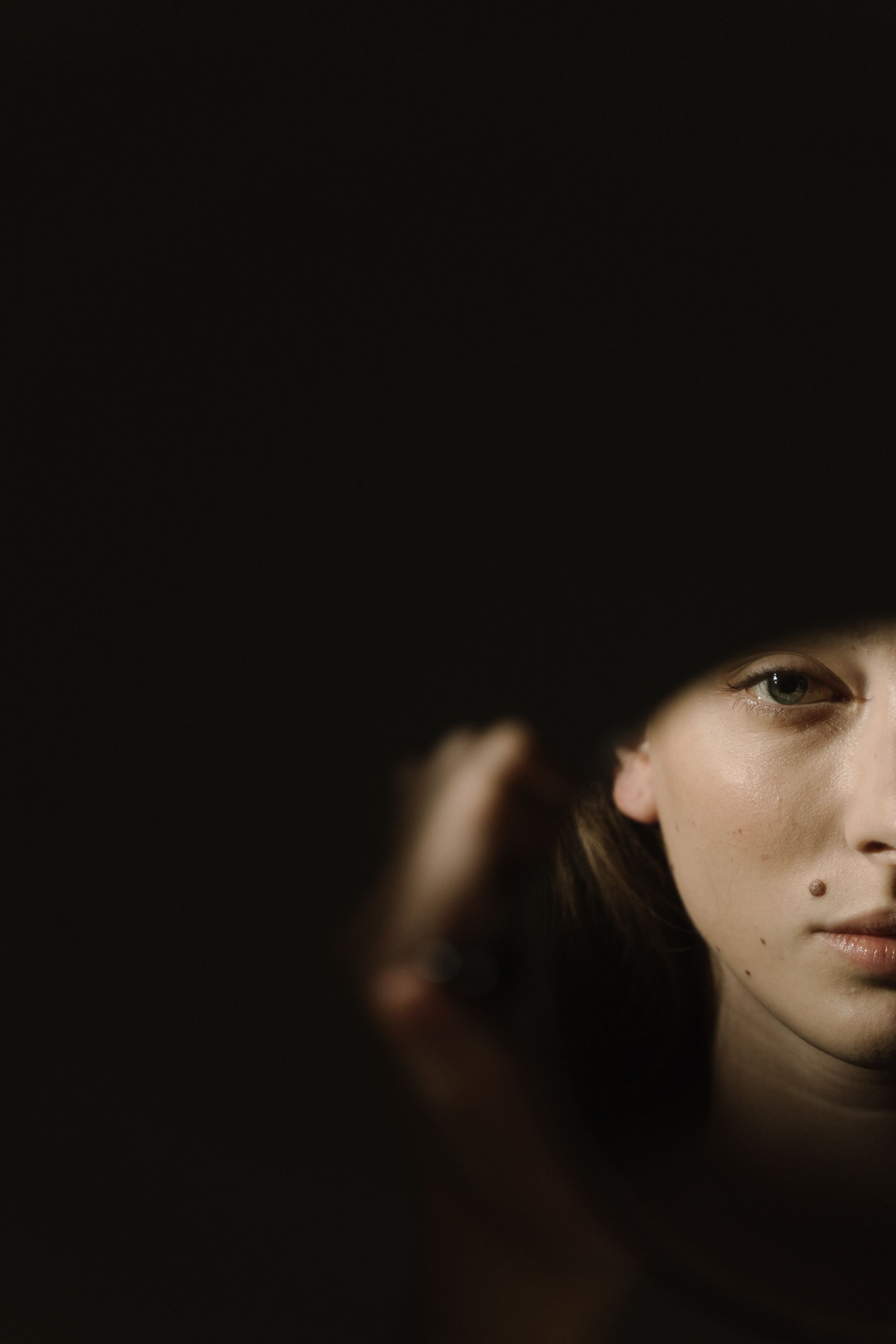 Close-up of a woman's face, showing her eye, eyebrow, nose, and mole with a dark background.