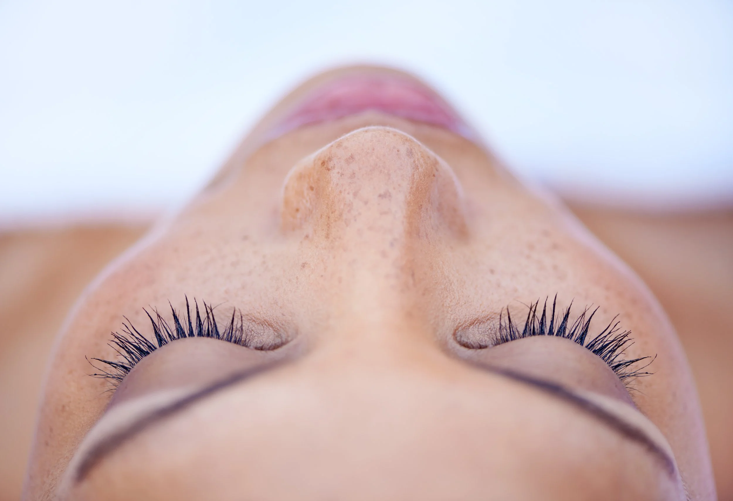 Close-up of a person's face upside down, showing closed eyes with long eyelashes, prominent nose, and smooth skin.