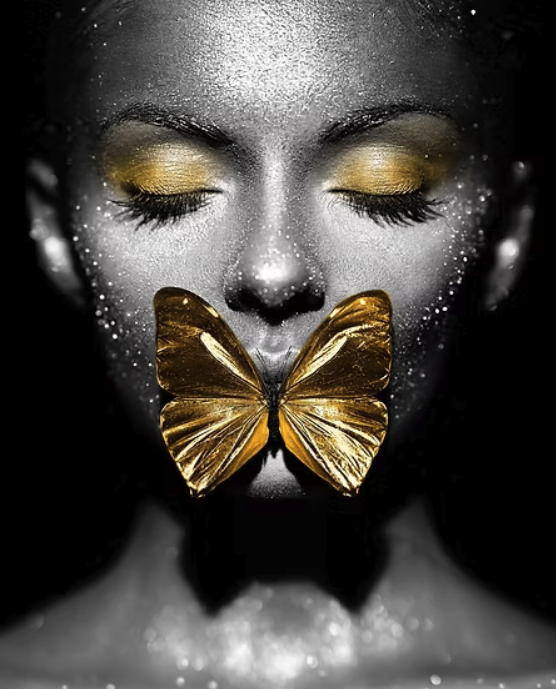 A close-up portrait of a woman with closed eyes, gold eyeshadow, glitter on her skin, and a large gold butterfly covering her lips.