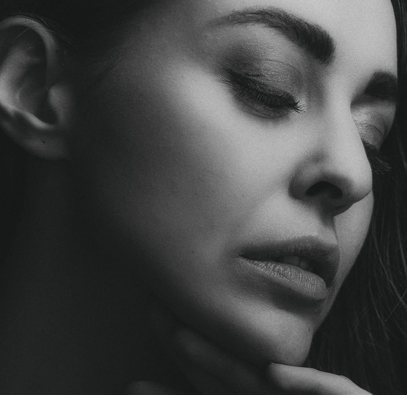 Close-up of a woman's face in black and white, showing her eye, eyebrow, nose, lips, and part of her cheek. She has smooth skin and dark hair.