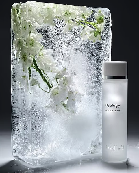A bottle of Hyalogy AC Clear Lotion next to an ice block with white flowers and ice inside.