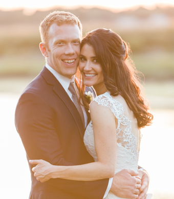 A happy couple in wedding attire smiling and embracing outdoors during sunset.