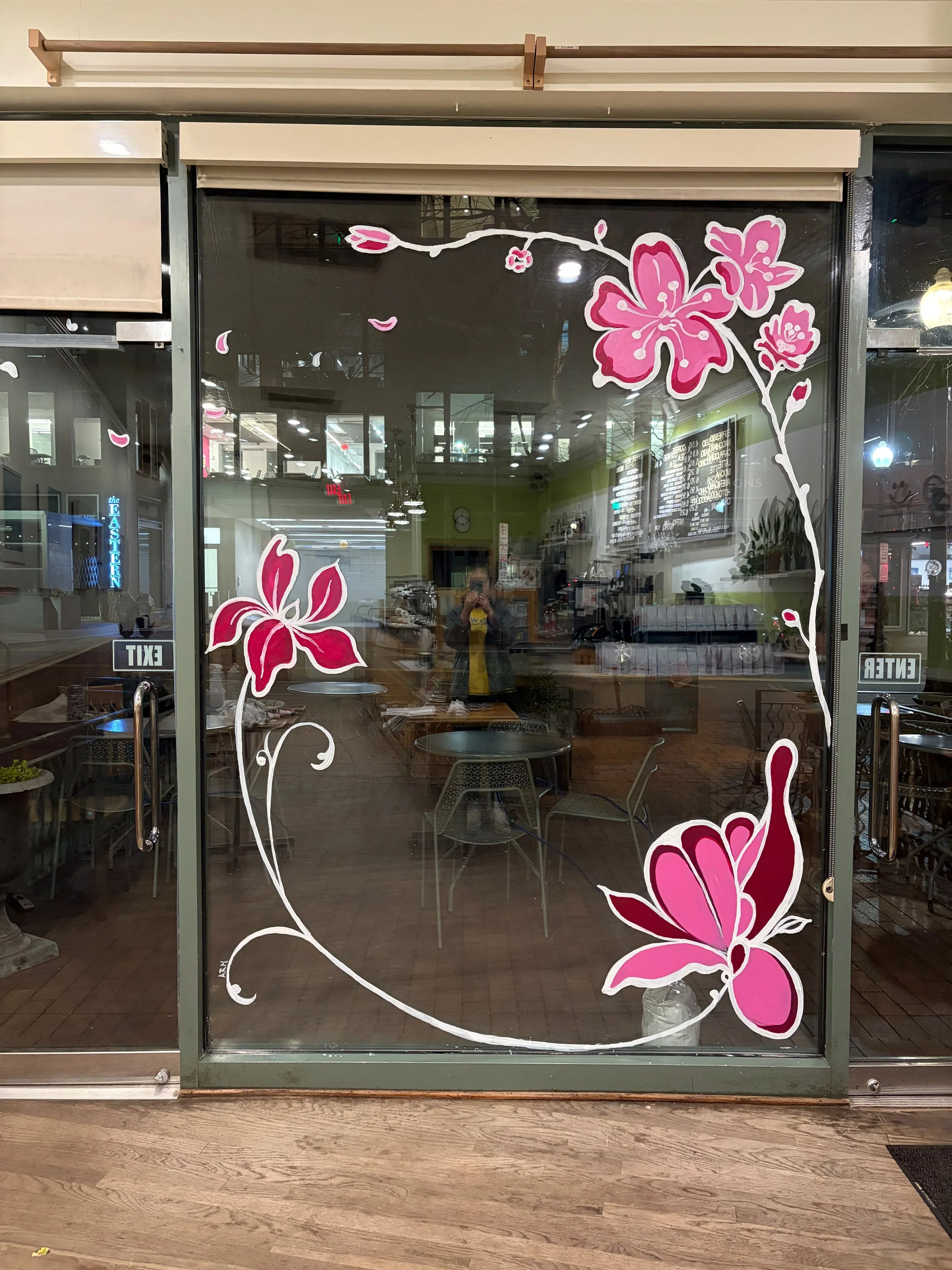 Glass door with pink and white floral decals, showing a reflection of the interior and exterior of a shopping mall or office building.