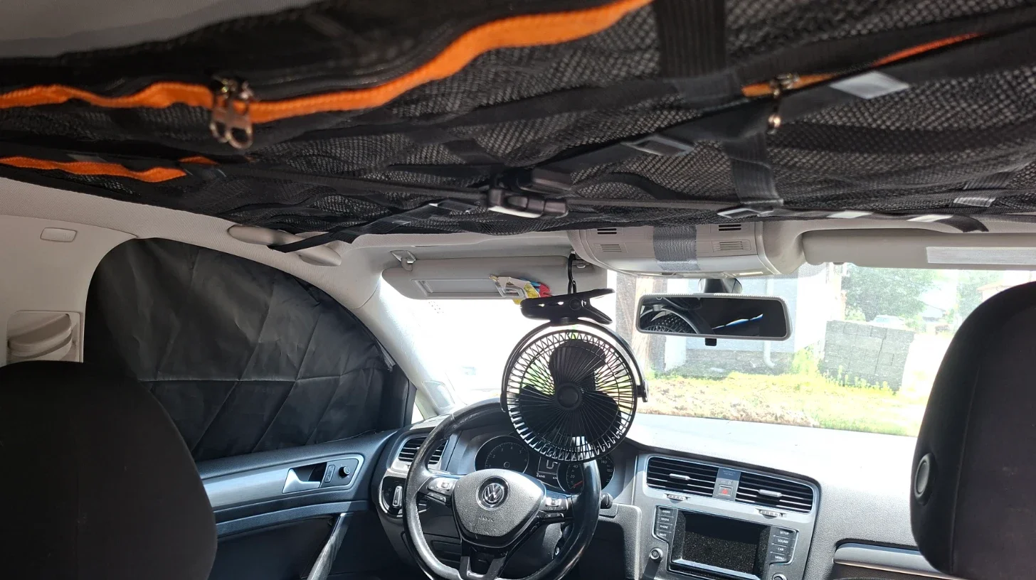 Portable USB fan attached to the driver's sun visor to improve ventilation while sleeping in a VW Golf Estate.