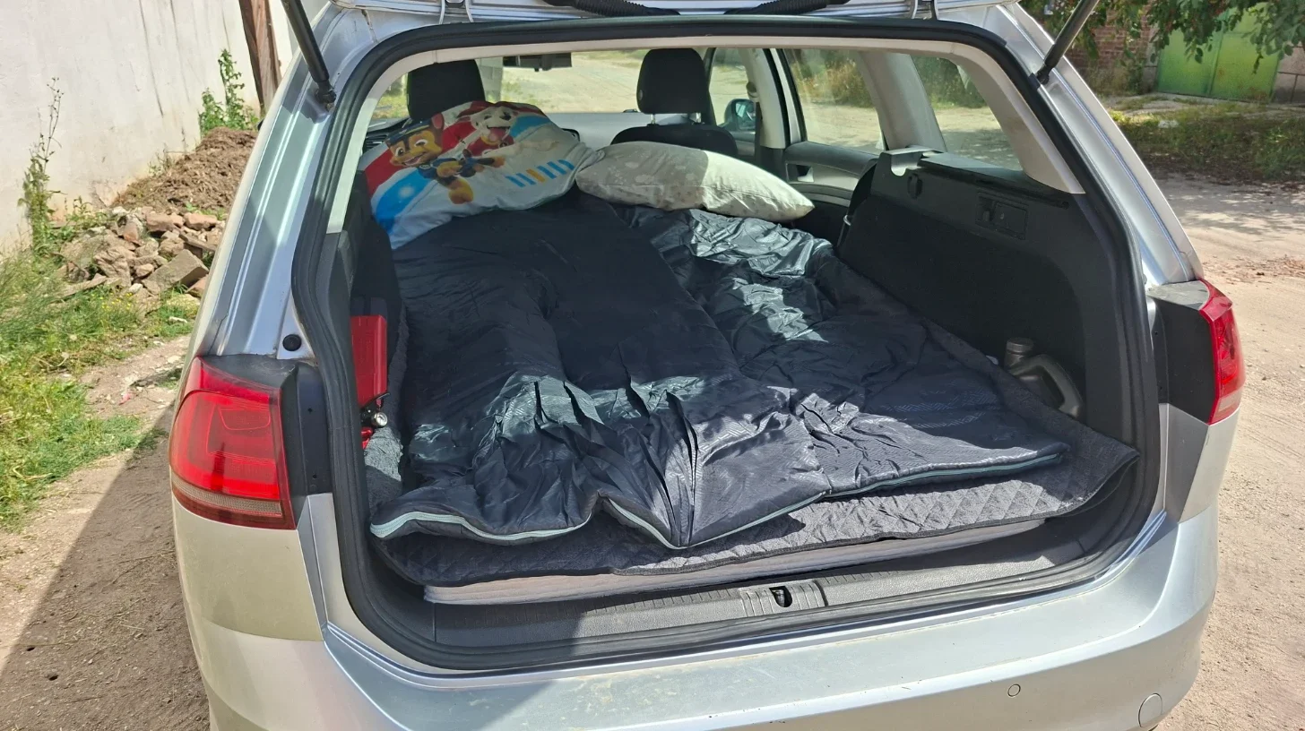 Fully deployed sleeping setup for two people inside a 2014 VW Golf Estate viewed from the rear hatch.
