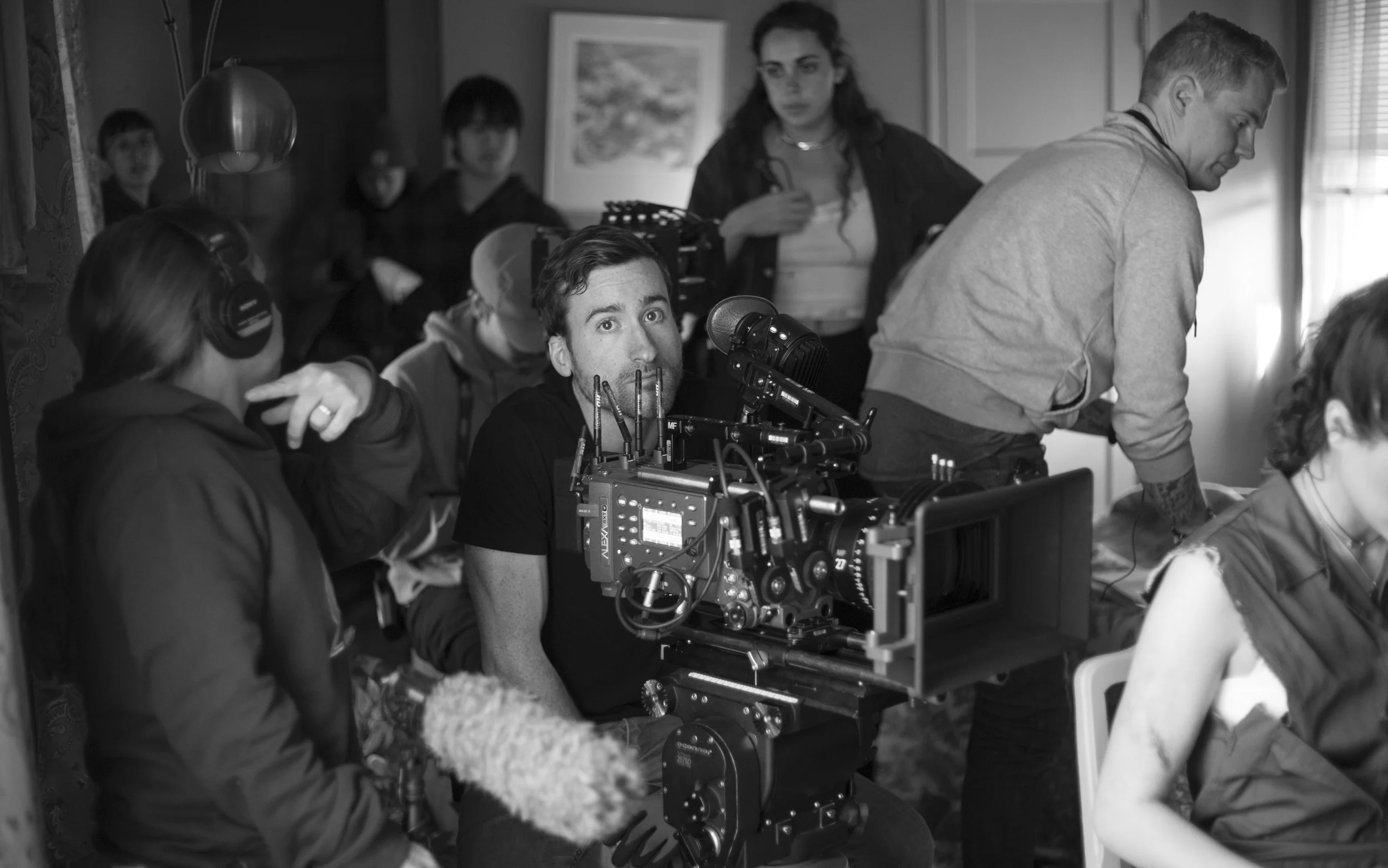 A film crew working on a set with a camera and multiple crew members gathered around, some looking at monitors and others preparing equipment.