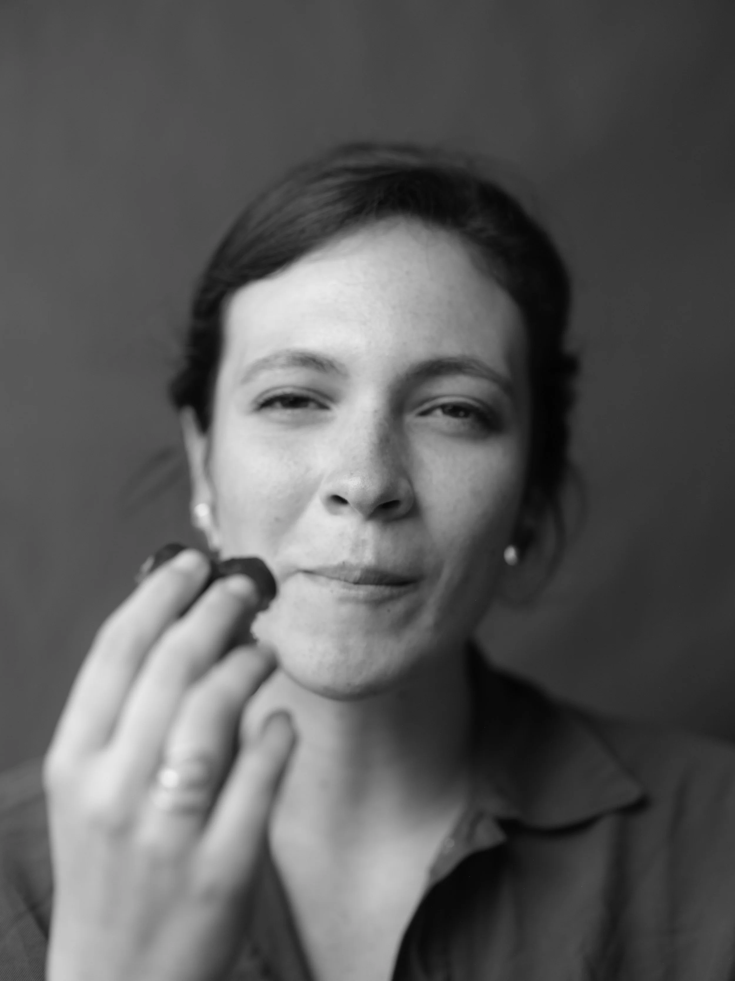 Black and white photo of a woman with short hair holding her hand up near her face, with a thoughtful expression.