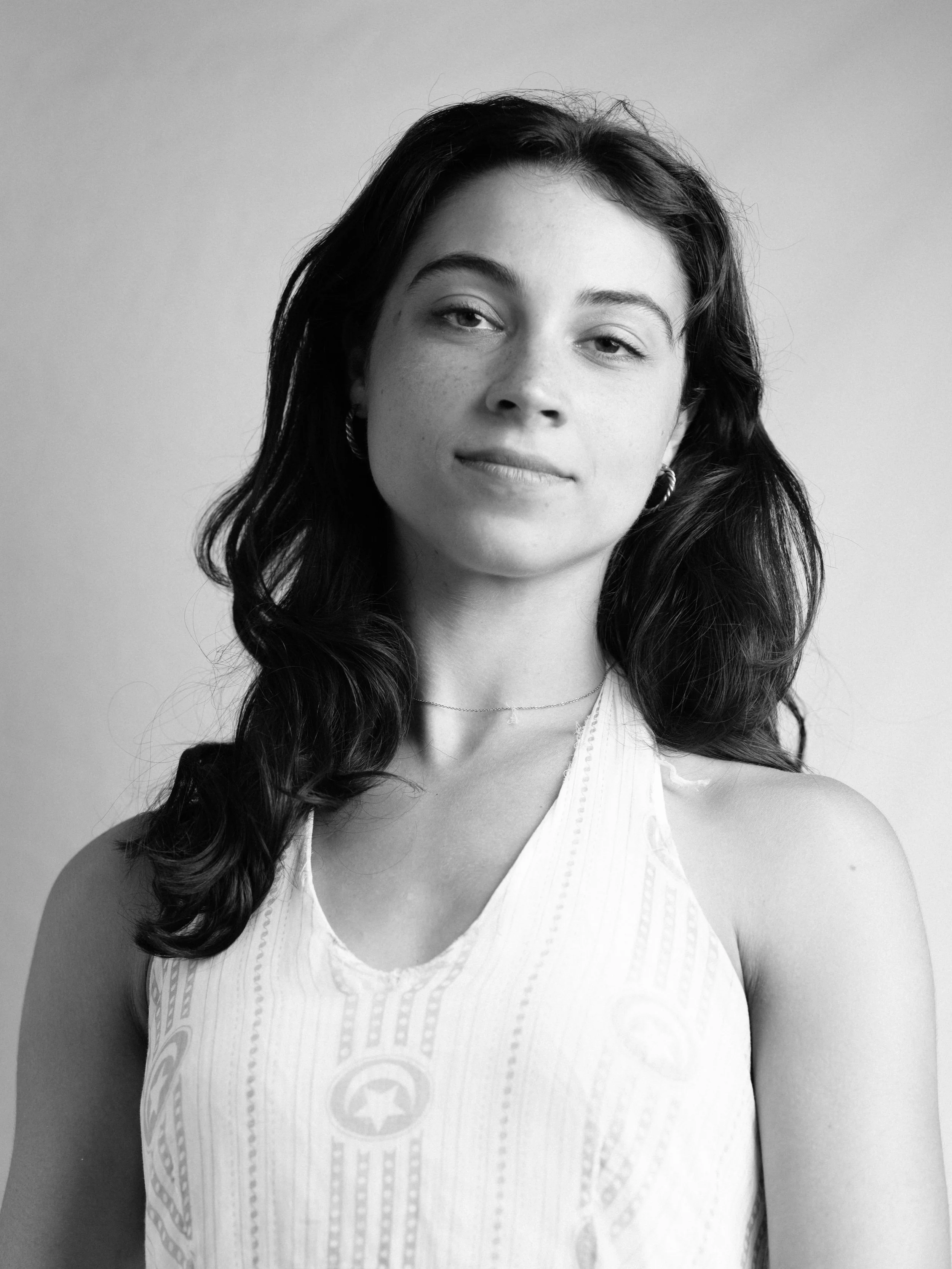 Black and white portrait of a woman with long wavy hair, wearing a sleeveless top with a star emblem and intricate patterns, and a thin necklace.