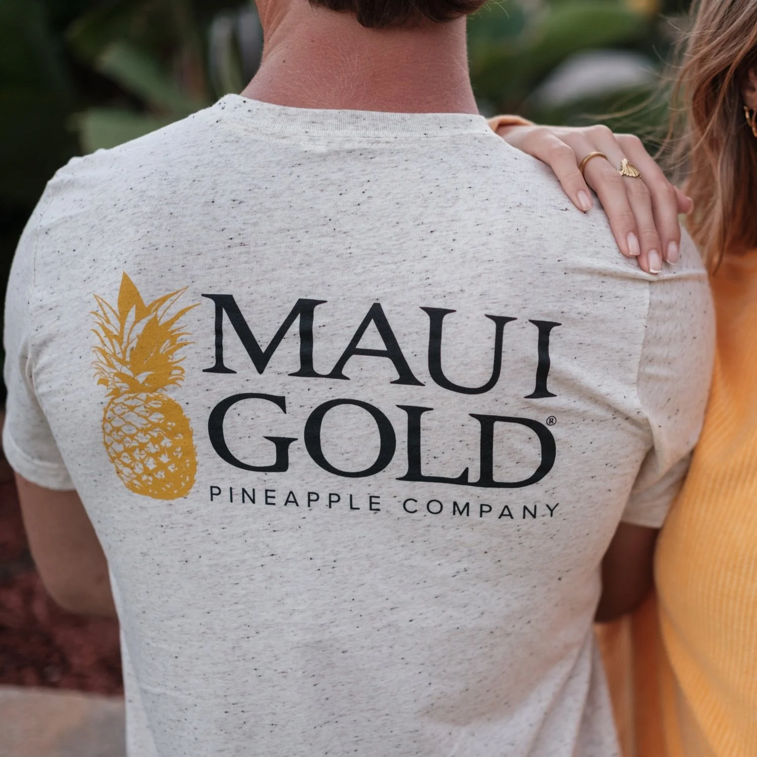 Person wearing a light-colored t-shirt with a gold pineapple graphic and the text 'Maui Gold Pineapple Company.'