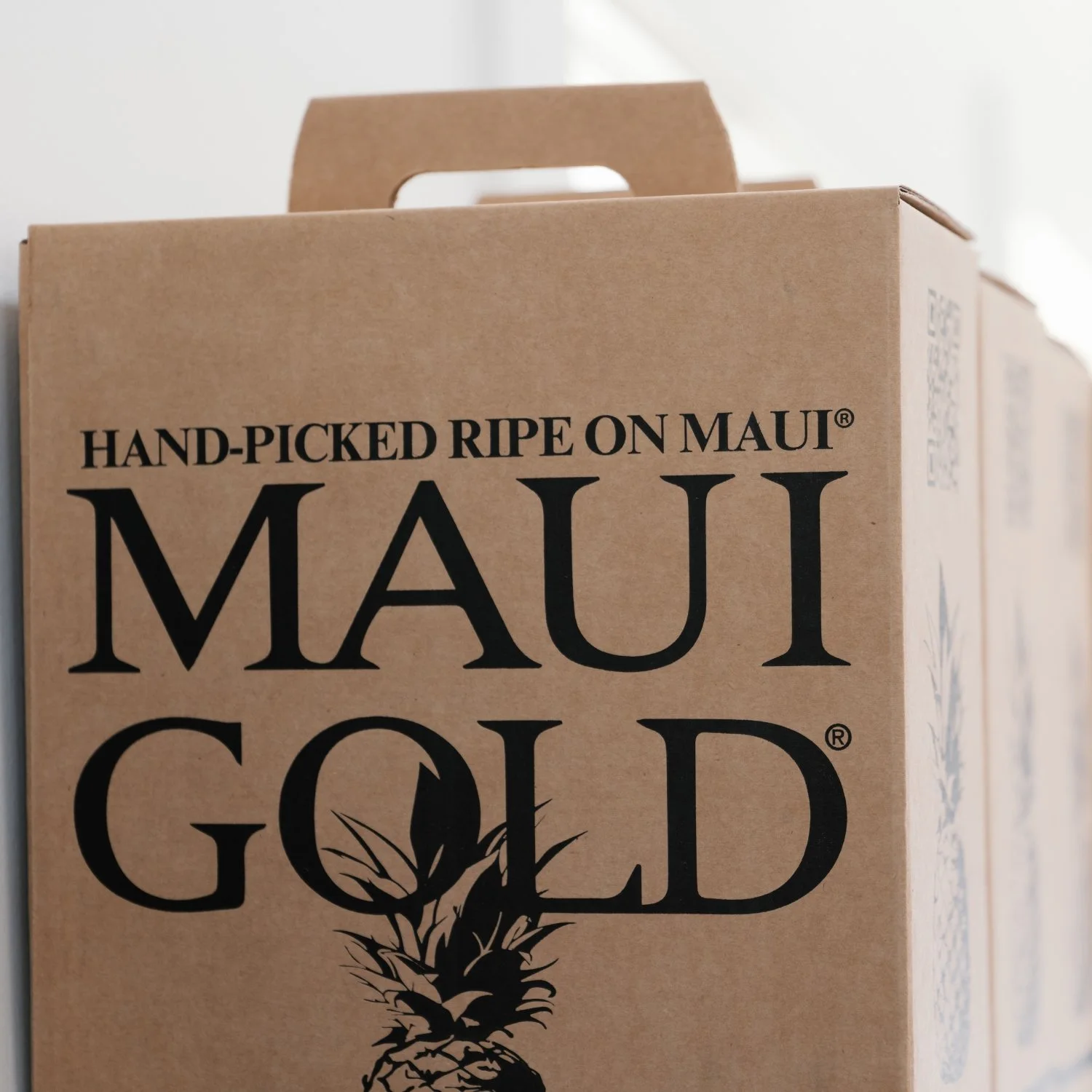 Brown cardboard box with a handle that reads, 'Hand-Picked Ripe on Maui' and 'Maui Gold' with an illustration of a pineapple.
