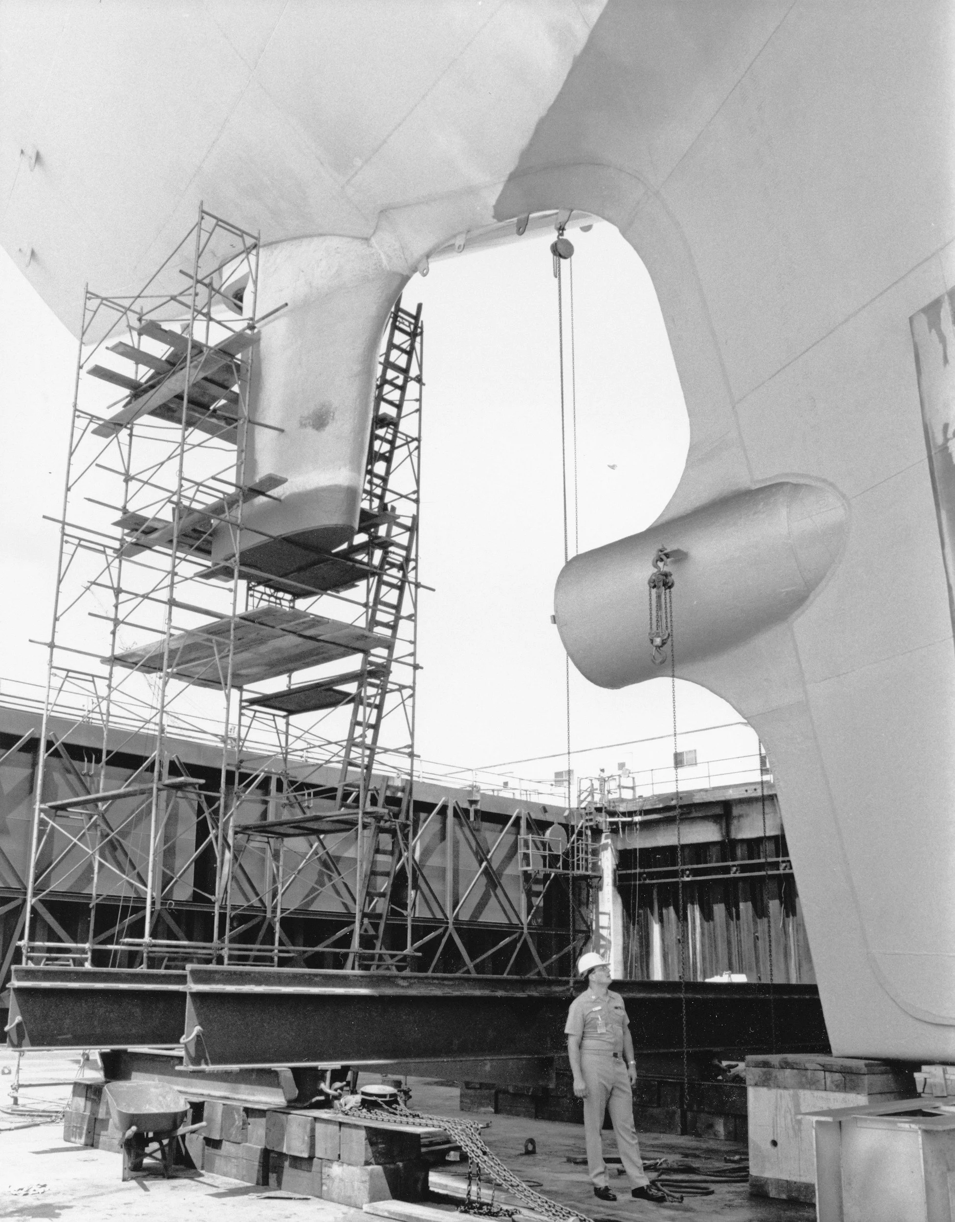 Construction workers and scaffolding around a large architectural structure, possibly a building or monument, with a woman in a hard hat observing.