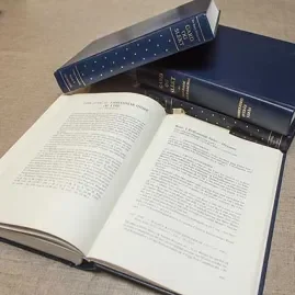 Open book with two closed books stacked on top, placed on a gray surface.