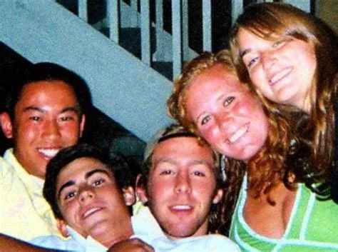 Group of five young friends smiling and posing closely together indoors.