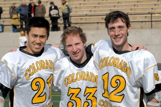 Three football players wearing Colorado uniforms with the numbers 21, 33, and 12, standing together on a football field after a game.