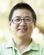 A smiling woman with glasses and short black hair outdoors, wearing a light green collared shirt.