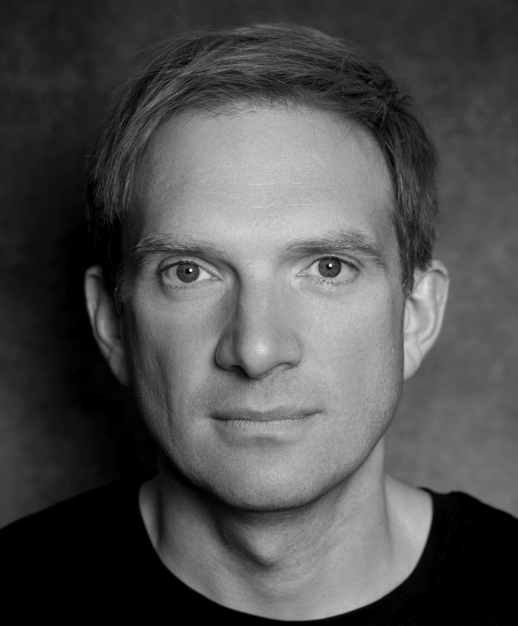 Black and white close-up photograph of a young man's face, focusing on his forehead, eyes, and nose, with a dark background. Andrey Burkovskiy.