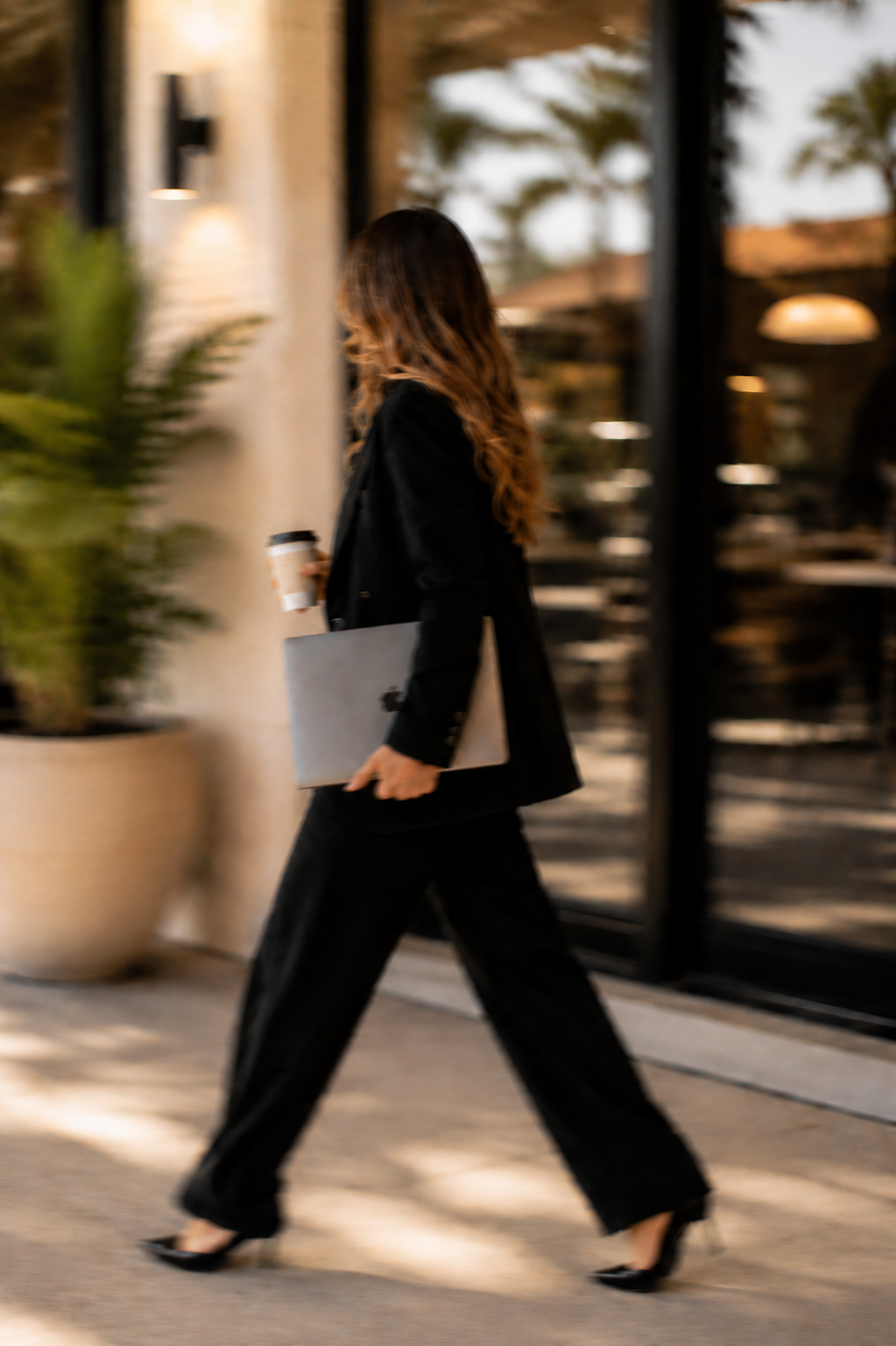 Woman walking by a coffee shop outside in Florida, holding a coffee and a laptop